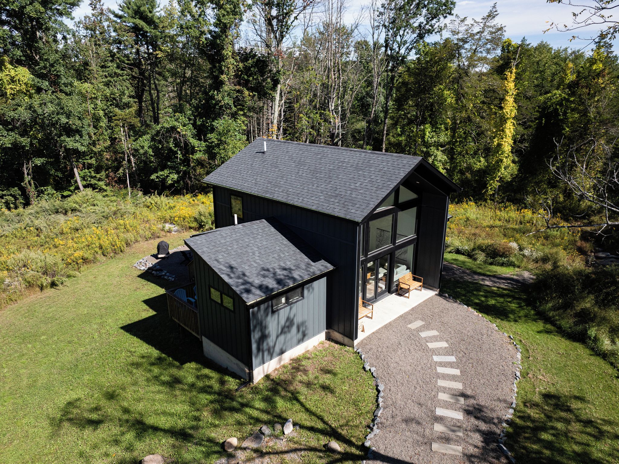 A modern two-story cabin with a large glass front, surrounded by a forested landscape.