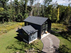 Een moderne, twee verdiepingen tellende blokhut met een grote glazen voorgevel, omgeven door een bebost landschap.