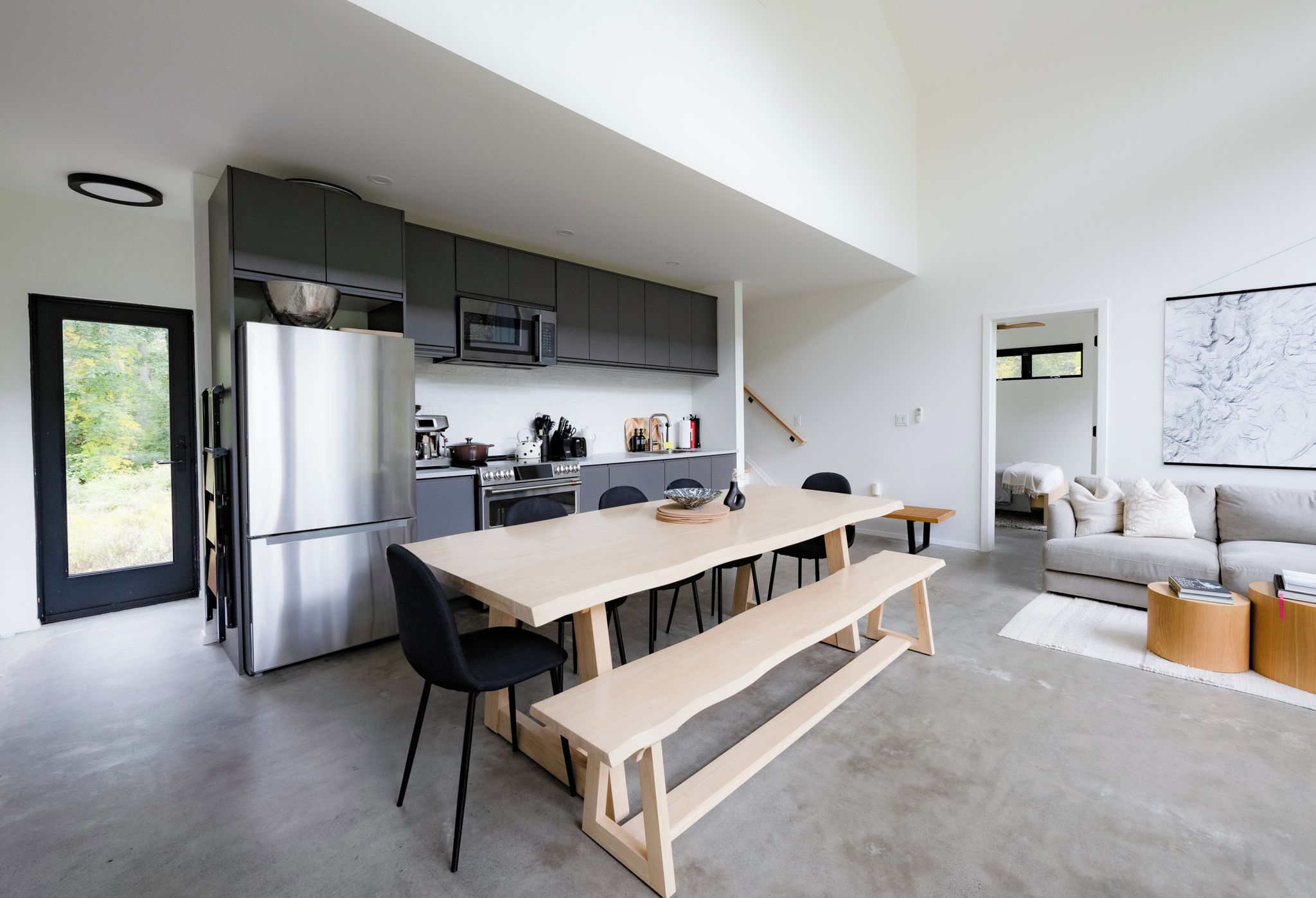 A modern kitchen with a central island, a dining area with a bench, and a living space with a sofa and a painting.