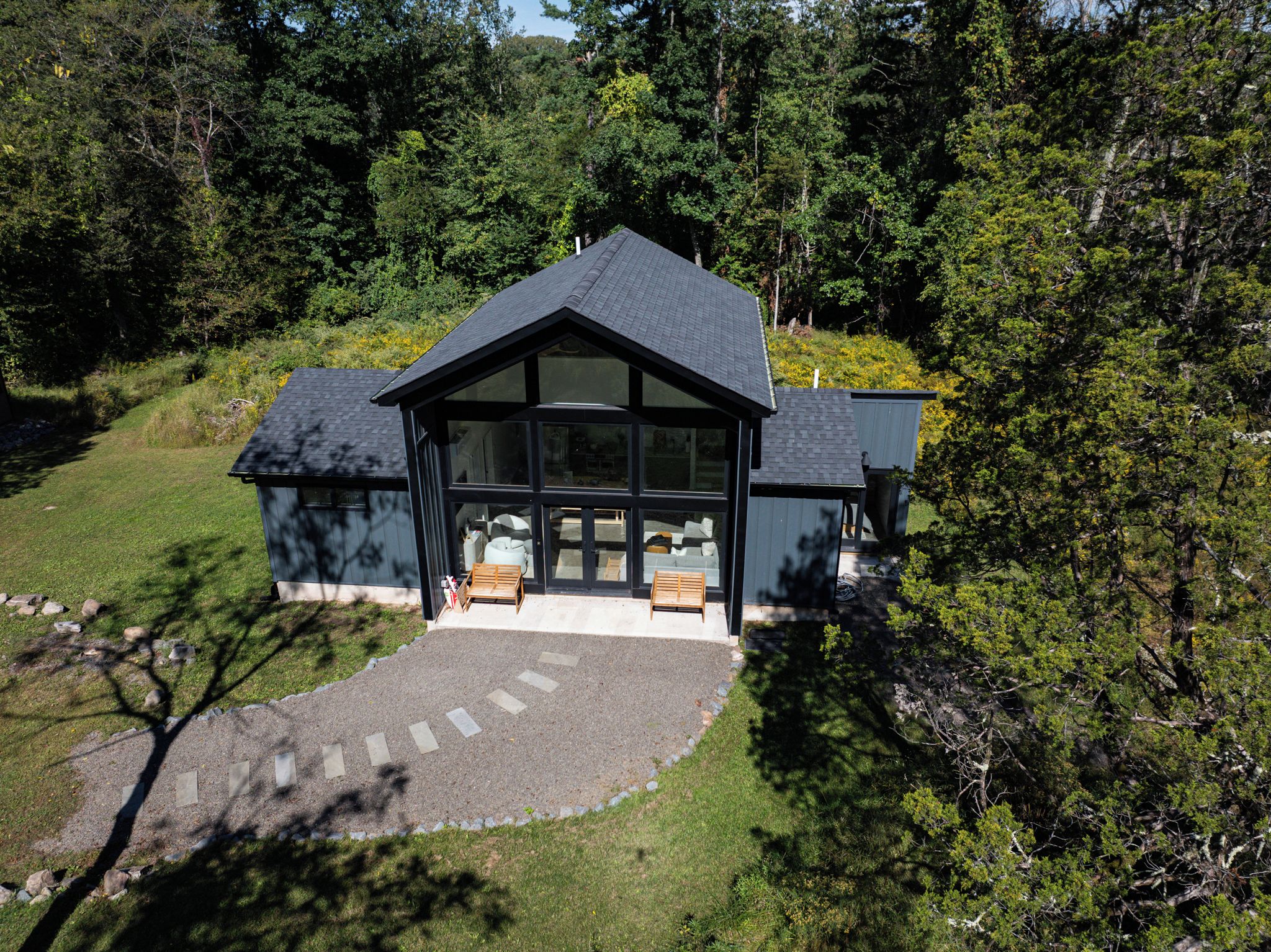 Ein modernes Haus mit großer Glasfront, einer überdachten Veranda mit zwei Holzbanken und einem gepflasterten Einfahrt.
