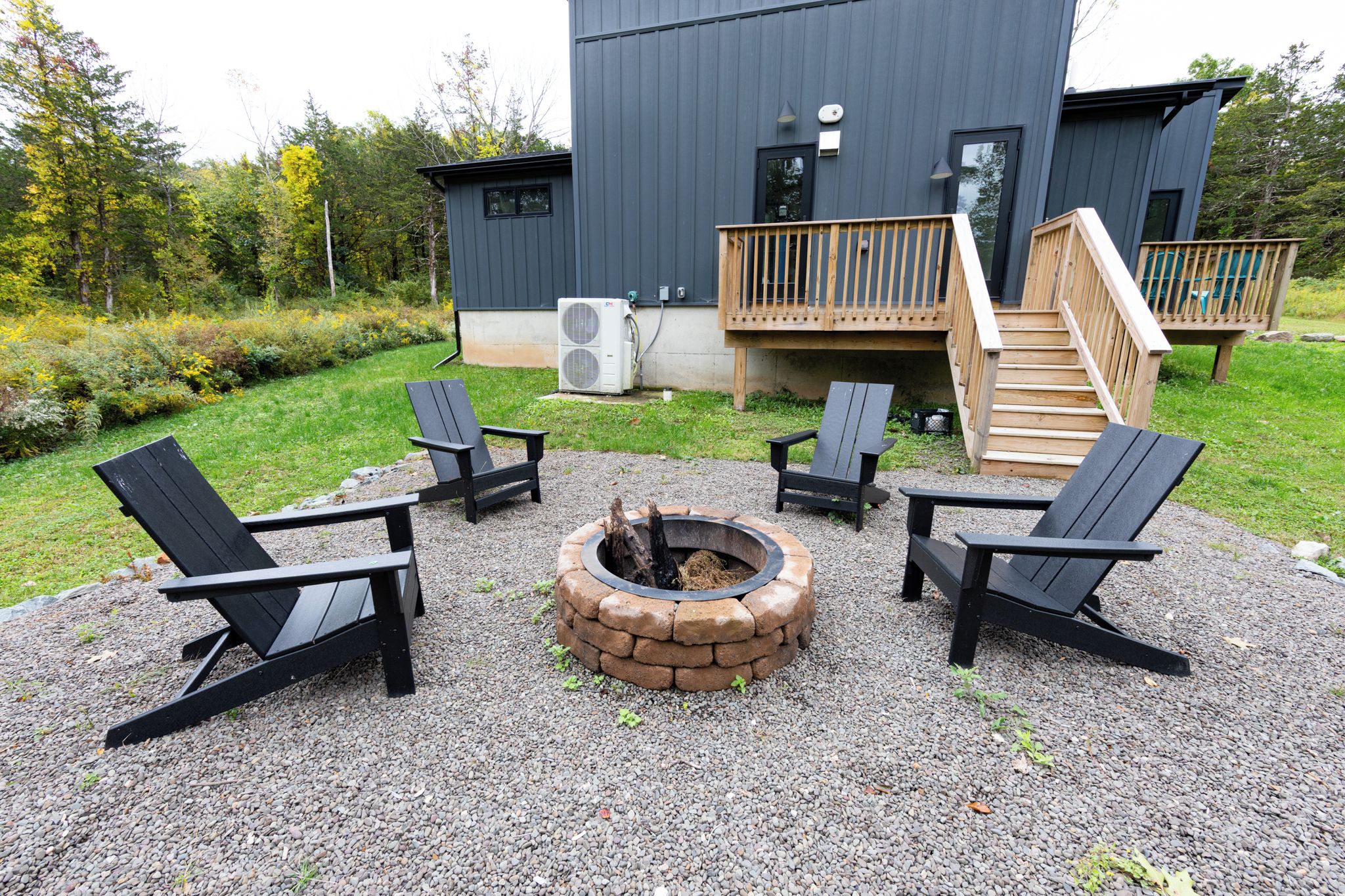 Un área de estar exterior moderna con sillas Adirondack y una chimenea, rodeada por un patio de grava.