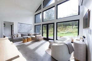 Een ruime woonkamer met een groot raam, een grijze bank en een ronde salontafel.