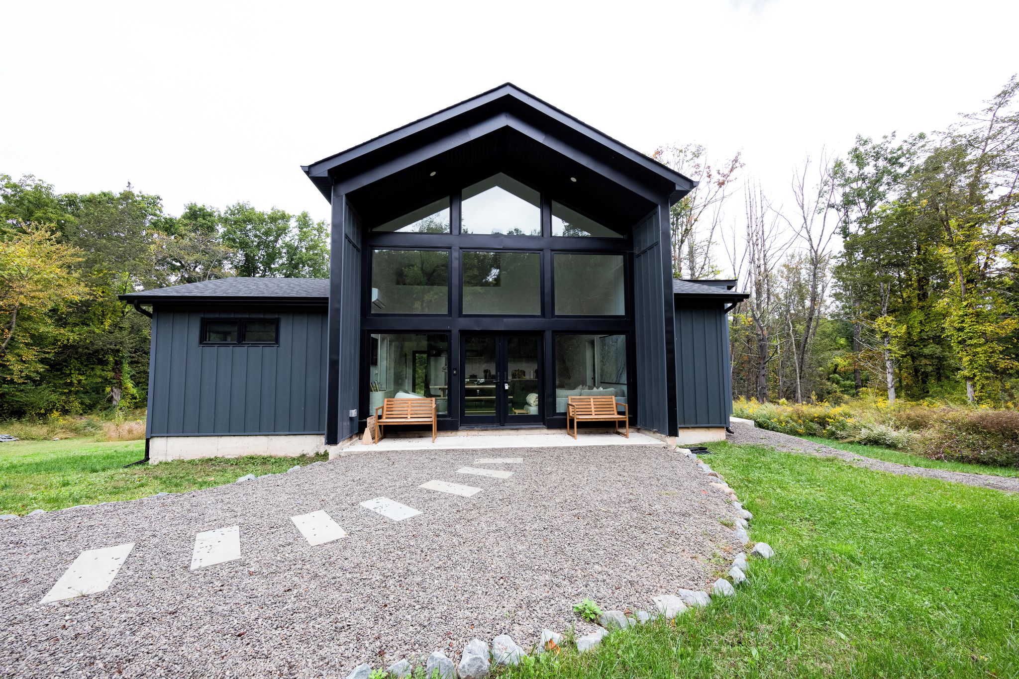 A modern building with a large glass facade, a gravel driveway, and two wooden benches in front.