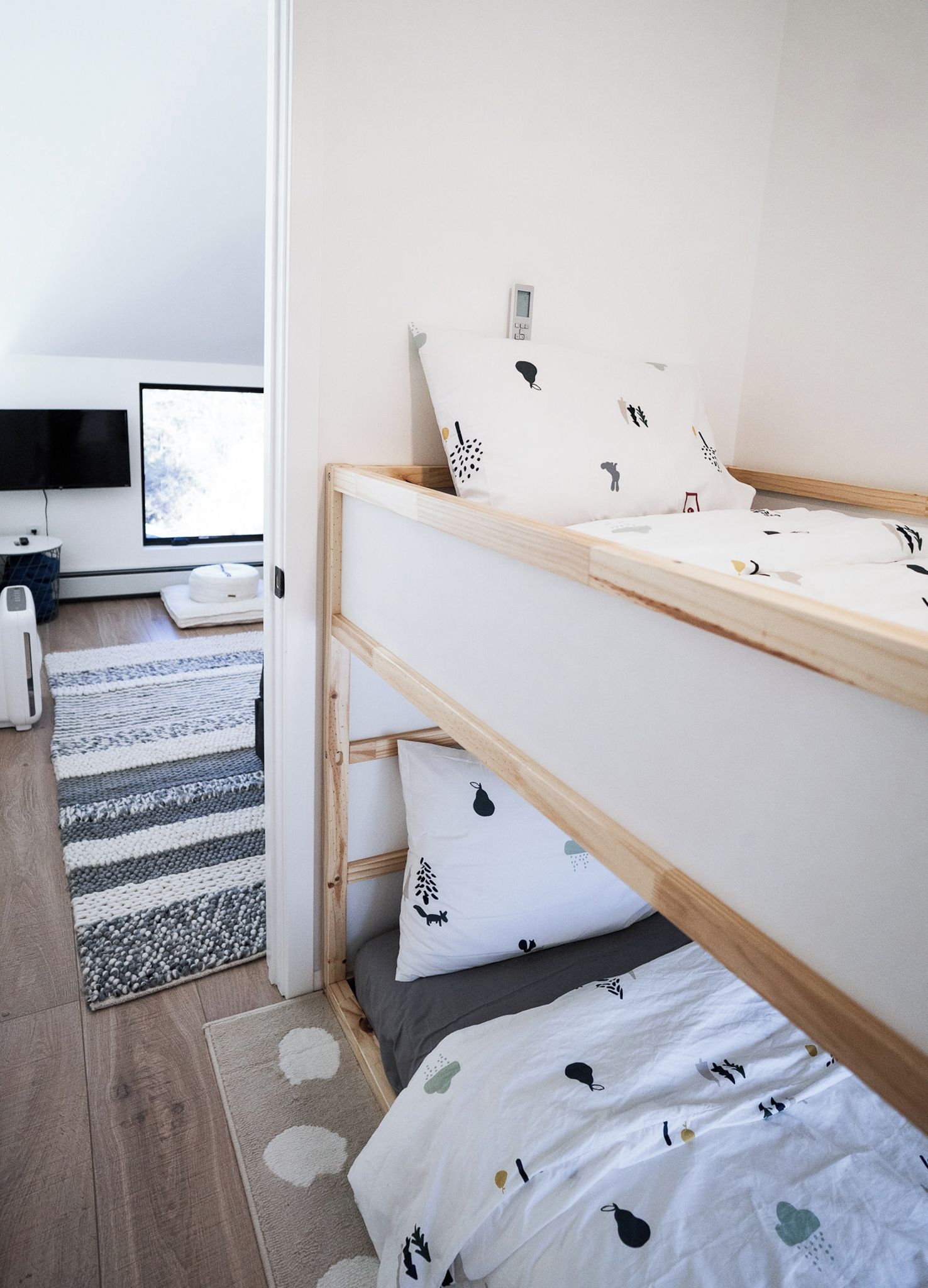 A bunk bed with white bedding and black patterns, a television, and a small table with a lamp.