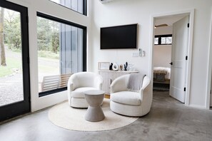 Een moderne woonkamer met twee fauteuils, een salontafel en een flatscreen televisie aan de muur.