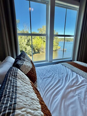 Quarto com uma grande janela que oferece vista para um lago e árvores.