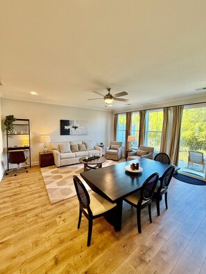 A spacious living room with a dining area, a ceiling fan, and a large window with curtains. - Lakefront Bliss on Lake Greenwood - 3BR Condo with Stunning Views (Greenwood)