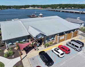 Ein Haus am Wasserufer mit überdachter Terrasse, Parkplatz und Blick auf das Wasser.
