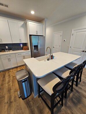 A modern kitchen with white cabinets, a stainless steel refrigerator, a sink, and a wooden floor. - Lakefront Bliss on Lake Greenwood - 3BR Condo with Stunning Views (Greenwood)