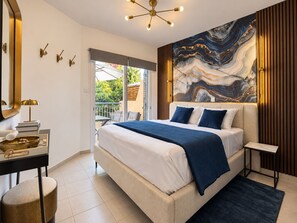 Ein modernes Schlafzimmer mit einem großen Bett, einem Nachttisch, einem Schreibtisch mit Lampe, einem Wandbild und Blick ins Freie.