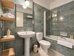 Ein Badezimmer mit Waschbecken, Toilette und Dusche. Handtücher und Pflegeprodukte befinden sich auf Regalen.