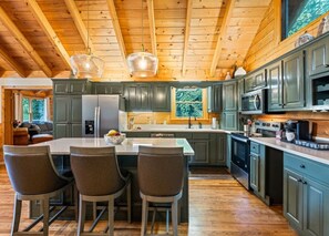 A kitchen with wooden beams, a central island with bar stools, and built-in appliances. - Rocky Top Retreat-Hot Tub, Game Room, Garage, View (Maggie Valley)