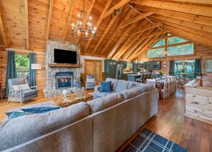 A spacious living area with a large sofa, a fireplace, and a dining area with wooden tables and chairs. - ROCKY TOP RETREAT - Perfect for Skiers and Holiday Travelers (Maggie Valley)