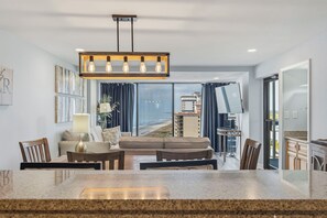 A modern living room with a large window, a dining area, and a kitchen. - Forest Dunes 1702 Penthouse · 3BR Ocean View (Myrtle Beach)