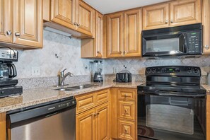 A kitchen with wooden cabinets, a microwave, a stove, a dishwasher, and a coffee maker. - Forest Dunes 1702 Penthouse · 3BR Ocean View (Myrtle Beach)