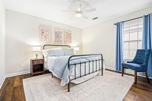 Een slaapkamer met een bed, nachtkastjes, een stoel, een plafondventilator en een raam met gordijnen.