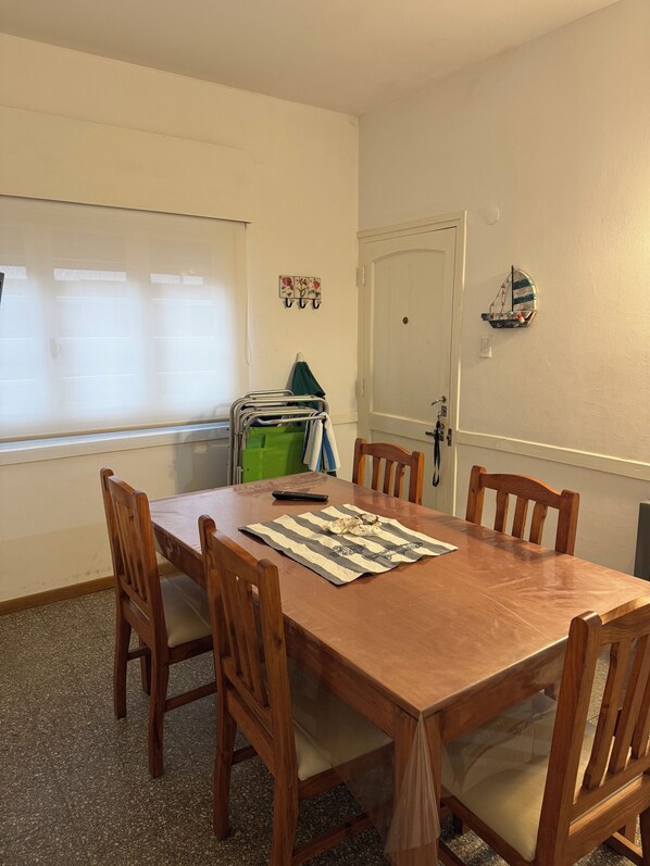 A dining area with a wooden table and chairs, a window with blinds, a coat rack, and a door.