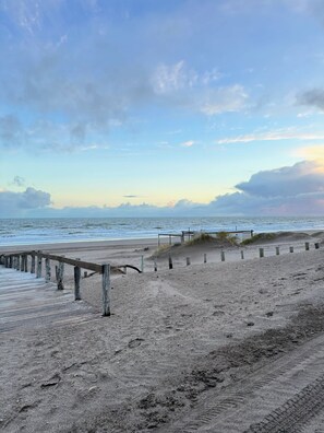 Une plage avec une promenade en bois menant à l’eau, un terrain sablonneux et un ciel nuageux.