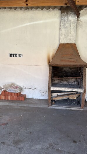 A rustic outdoor area with a brick oven, a wooden beam structure, and a wall with a 'DTO' sign.