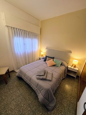 A hotel room with a bed, two bedside tables, a chair, and a window with curtains.