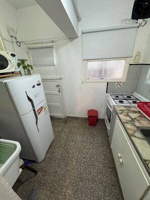 A compact kitchen with a refrigerator, stove, and a small window.