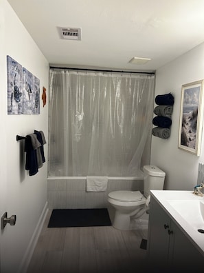 A bathroom with a bathtub, toilet, and sink. There are towels hanging on the wall and a shower curtain. - Chasing Sunsets
Cozy 1-bedroom  2 bath  with 2 beds and All new furnishings. (Galveston)