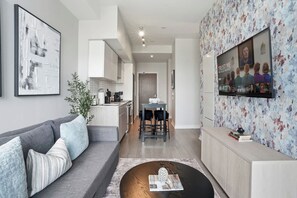 A modern living room with a grey sofa, a coffee table, and a TV mounted on the wall. - City View Condo, Walk to Eaton Centre, Sleeps 6! | Parking Available (Toronto)