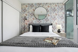 A bedroom with a large bed, a round mirror above it, and a floral wallpaper. - City View Condo, Walk to Eaton Centre, Sleeps 6! | Parking Available (Toronto)
