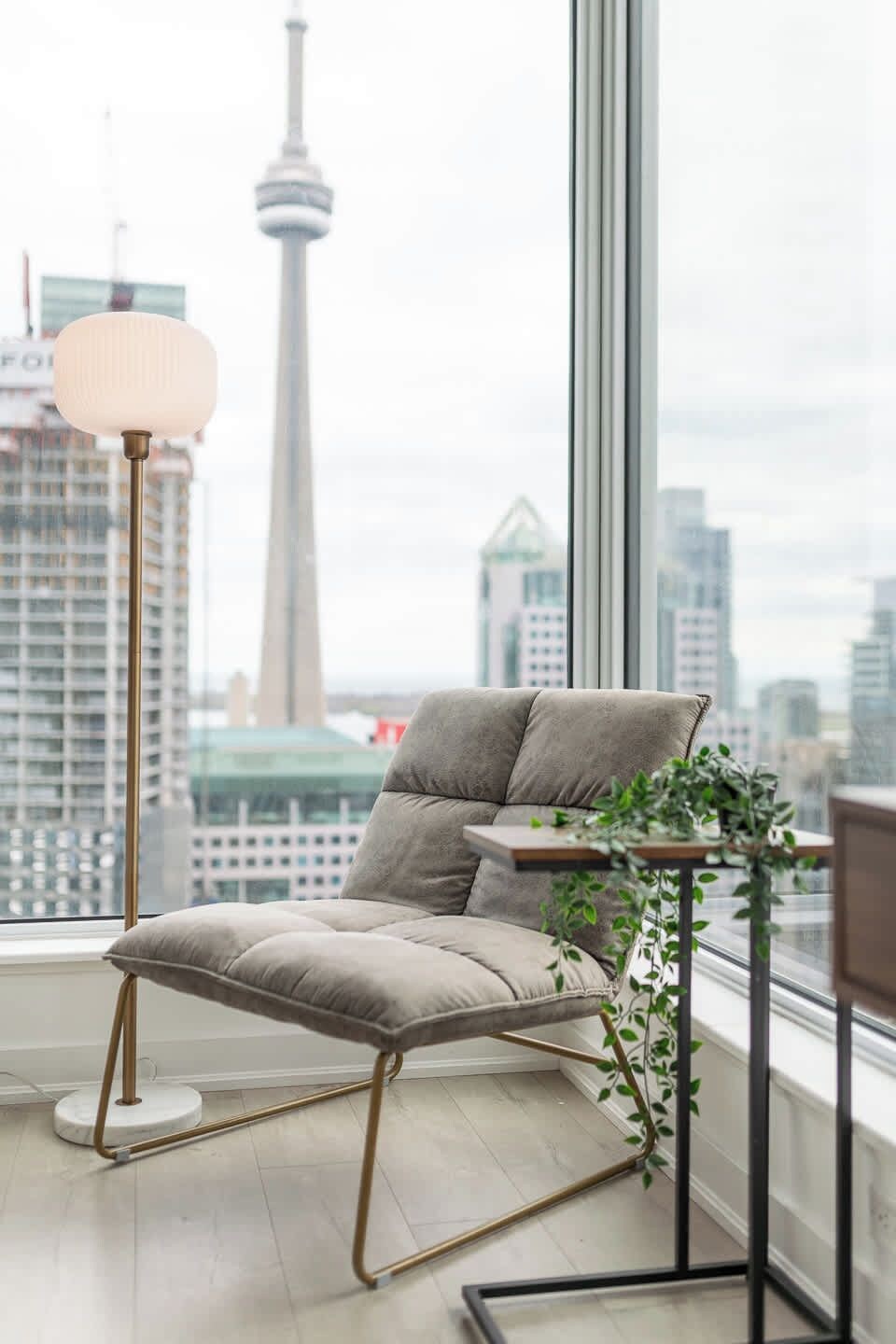 A modern chair with a cushioned seat and backrest, positioned next to a window with a view of a city skyline and a tower.