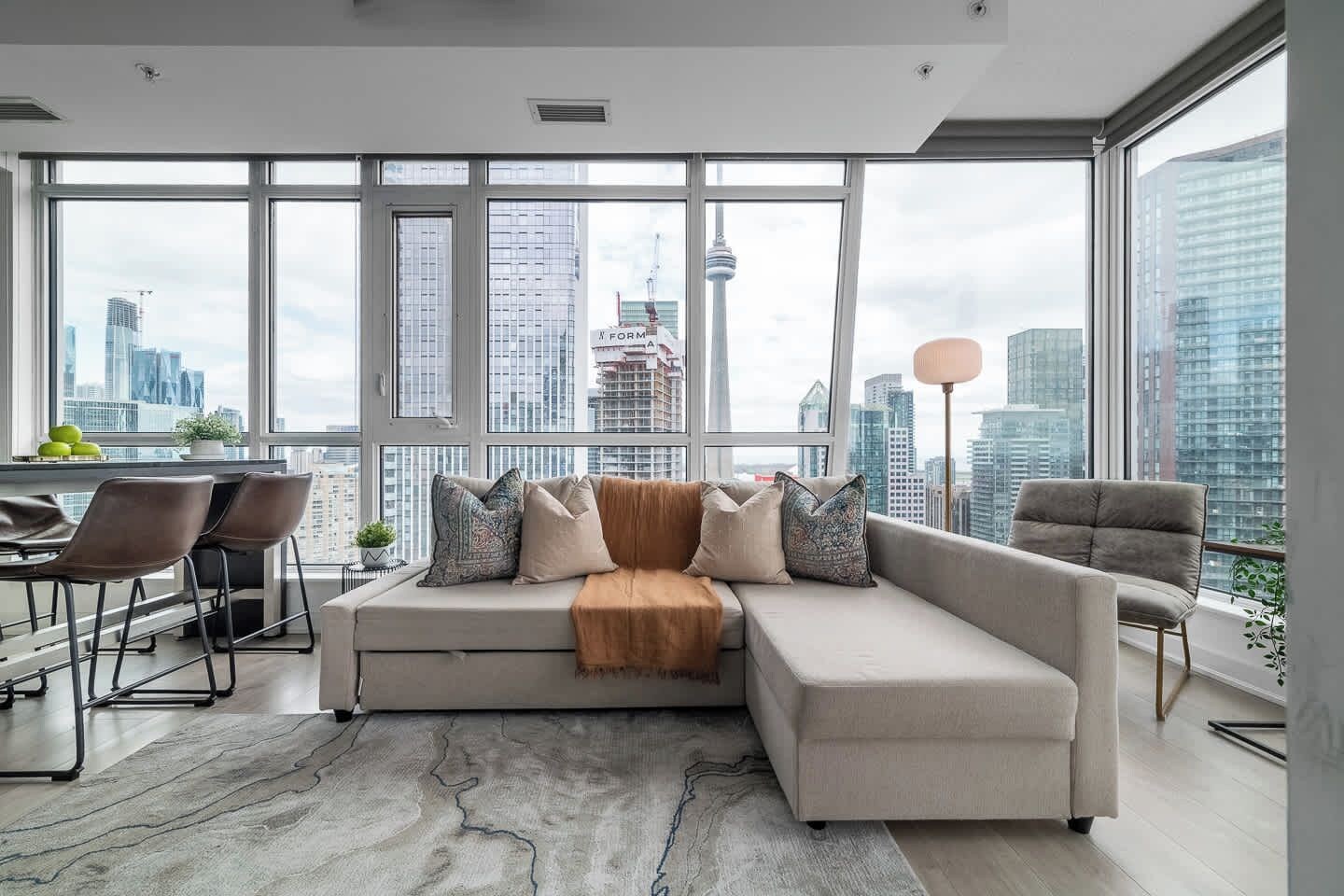 A modern living room with a sectional sofa, a dining area with chairs, and large windows offering a city view.