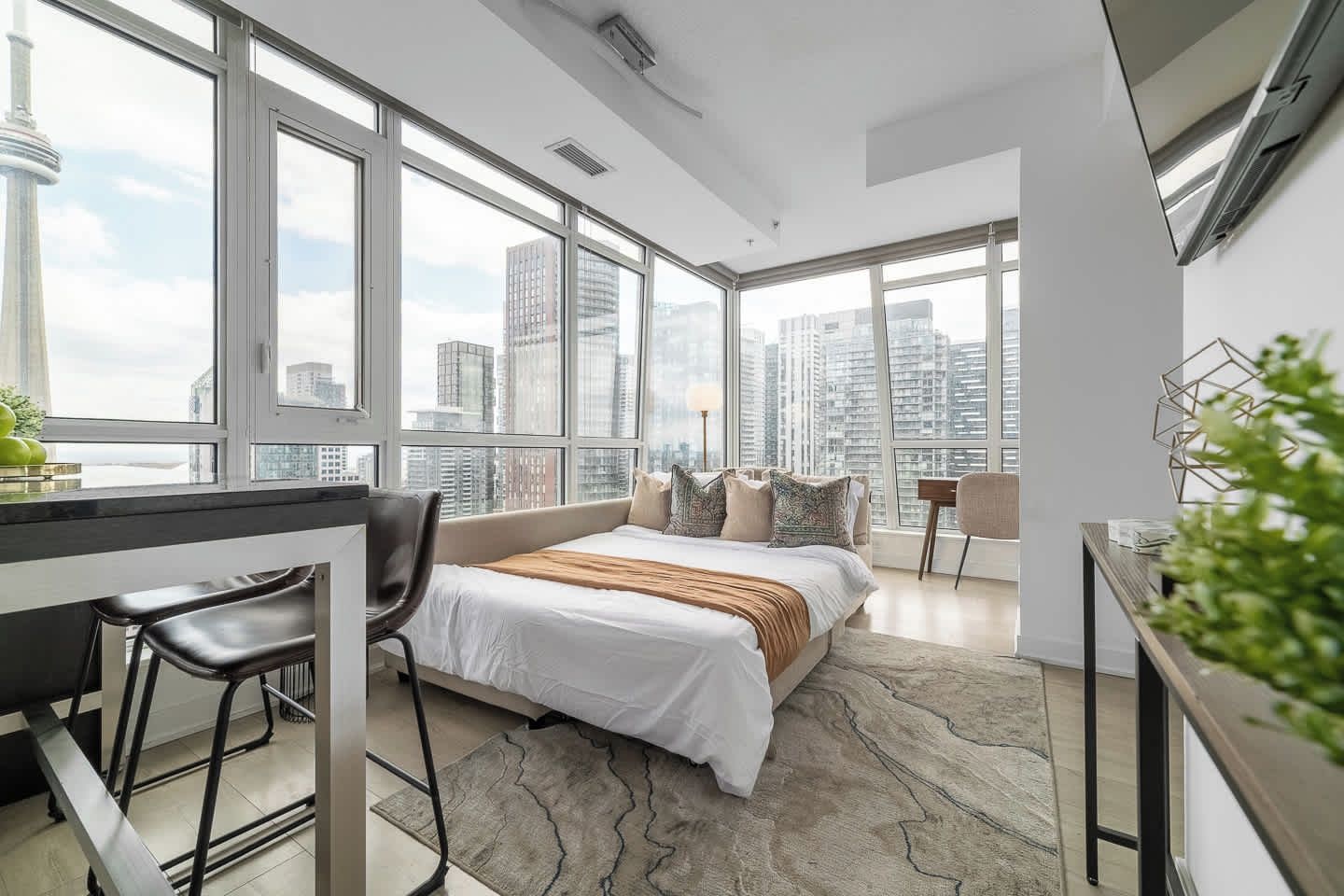 A modern hotel room with a large bed, a desk, and a view of the city skyline.