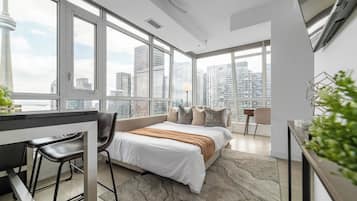 A modern hotel room with a large bed, a desk, and a view of the city skyline.