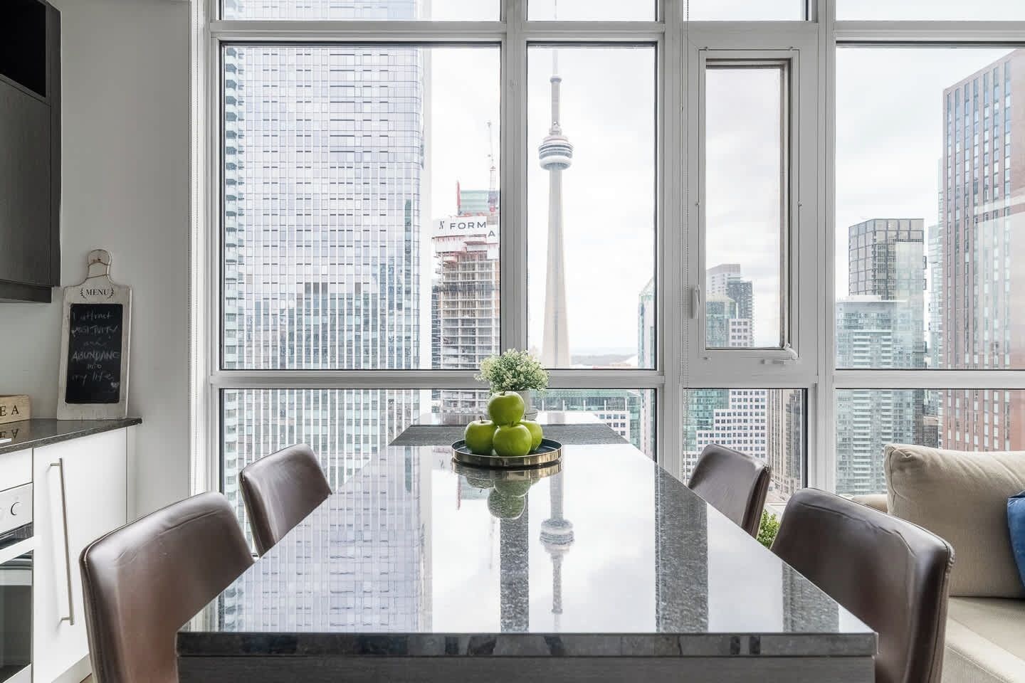 A modern dining area with a large window, a marble table, and a view of a cityscape including a tower.