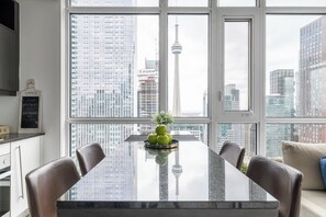 A modern dining area with a large window, a marble table, and a view of a cityscape including a tower. - CN Tower Views, Gym, Hot Tub, Prime Location (Toronto)