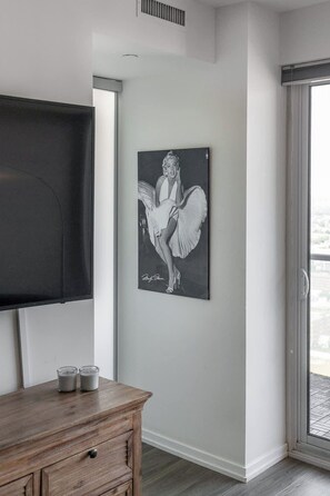 A room with a flat-screen TV mounted on the wall, a wooden dresser with two glasses, and a framed black and white portrait of a woman. - Modern Cozy Condo in the Heart of Toronto! | Parking Available (Toronto)