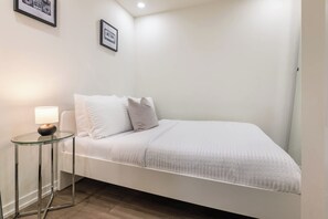 A minimalist room with a bed, a bedside table with a lamp, and two framed pictures on the wall. - Modern Cozy Condo in the Heart of Toronto! | Parking Available (Toronto)