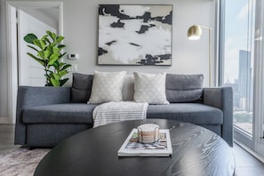 A modern living room with a gray sofa, a round coffee table, and a large abstract painting on the wall. - City View Condo, Walk to Eaton Centre, Sleeps 6! | Parking Available (Toronto)