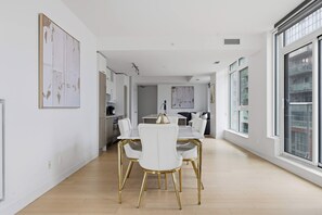 A modern kitchen with white cabinets and a dining area with a white table and gold chairs. - CN Tower View 2BR/2BA | Free Parking Included | Parking Available (Toronto)