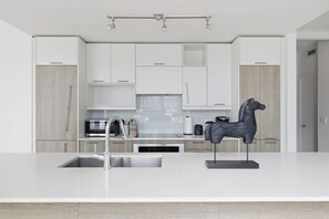 Een moderne keuken met witte kasten, een roestvrijstalen spoelbak, een magnetron en een decoratief paardbeeld.