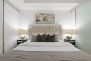 A modern bedroom with a tufted headboard, a painting above the bed, and two bedside lamps. - CN Tower View 2BR/2BA | Free Parking Included | Parking Available (Toronto)