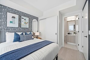 Ein modernes Schlafzimmer mit einem großen Bett, einem Nachttisch, einem Spiegel und einem durch eine offene Tür einsehbaren Badezimmer.