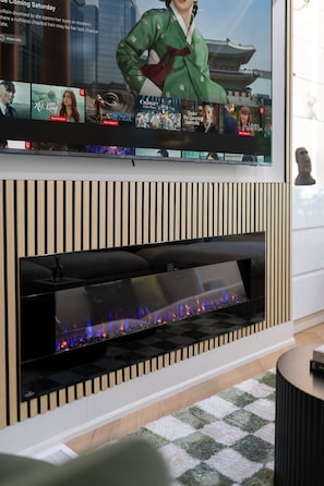 Un salon moderne avec un téléviseur à écran plat fixé au-dessus d’une cheminée dotée d’une façade en verre.