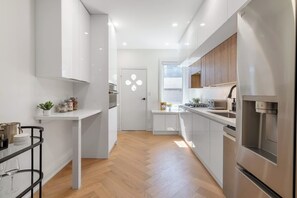 A modern kitchen with white cabinetry, stainless steel appliances, and a herringbone wood floor. - Designer Trinity Bellwoods Gem Sleeps 12 Arcade | Parking Available (Toronto)