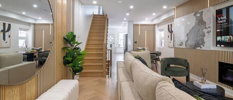 A modern living room with a sofa, a coffee table, and a TV. There is a staircase leading to another level.
