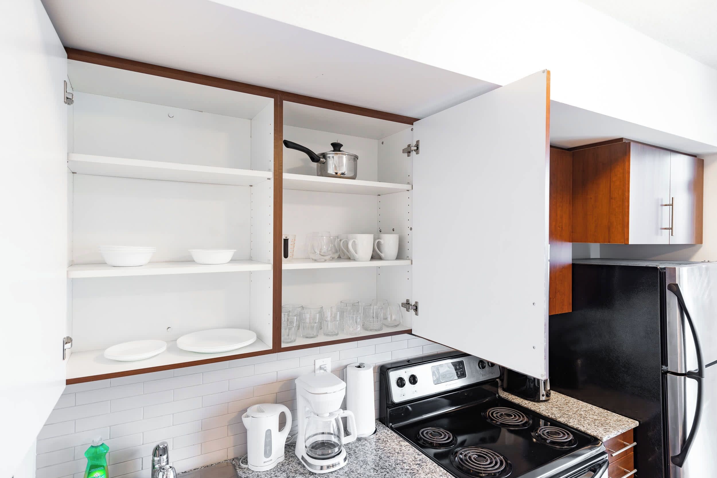 A kitchen with a stove, coffee maker, and open cabinets.