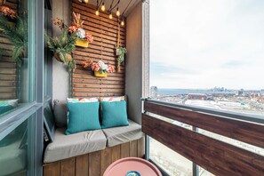 A balcony with a wooden slat wall, a cushioned bench with teal cushions, and a view of a cityscape. - Luxe Downtown 1BR Suite, Workspace & 55" TV (Toronto)