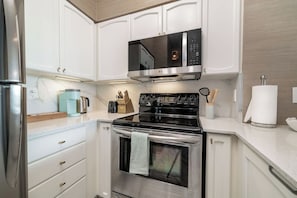 A modern kitchen with white cabinetry, stainless steel appliances, and a built-in microwave. - Luxe Downtown 1BR Suite, Workspace & 55" TV (Toronto)