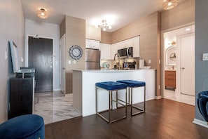A modern kitchen with a central island, stainless steel appliances, and a clock on the wall. - Luxe Downtown 1BR Suite, Workspace & 55" TV (Toronto)