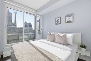 A modern bedroom with a large bed, a view of the city through floor-to-ceiling windows, and a minimalist decor. - Stylish TO Condo CN Tower View Walk Score 99 | Parking Available (Toronto)
