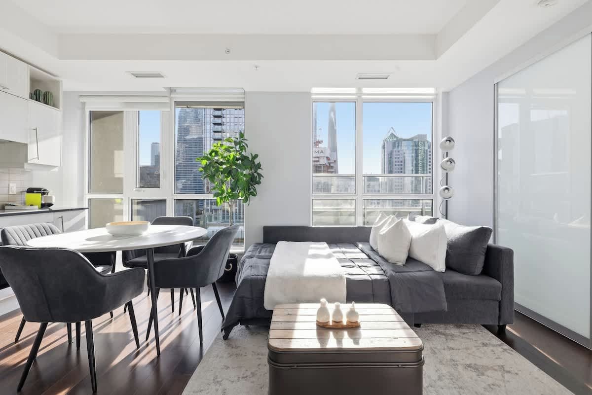 A modern living space with a dining area, a sofa, and a view of the cityscape.